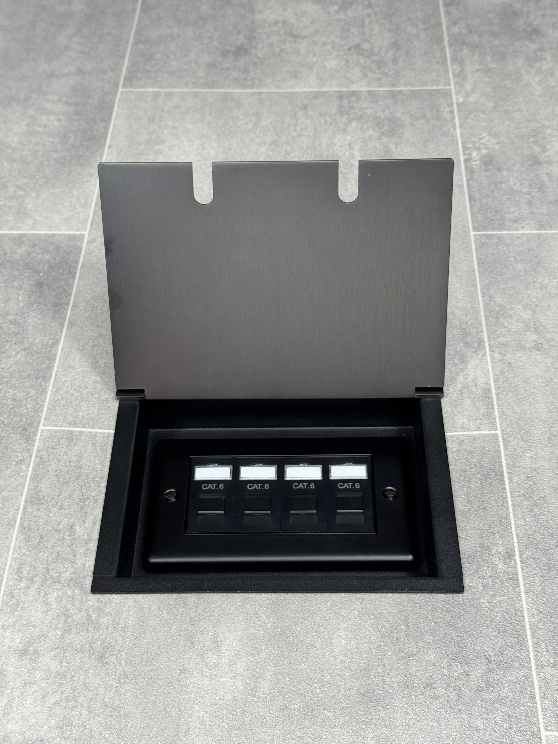Old bronze double recessed floor socket with a black base installed on a grey floor, opened to show the 4 gang RJ45 cat6 socket.