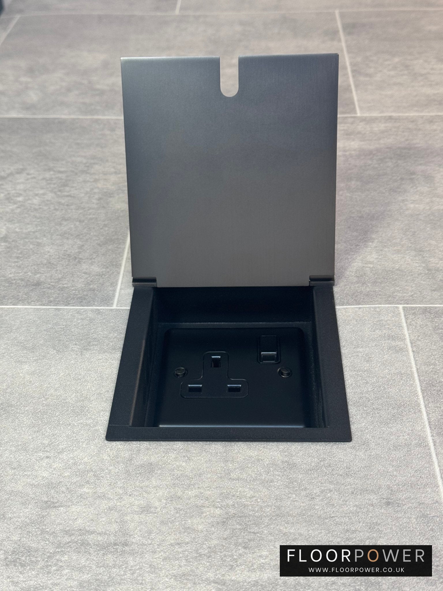 Old bronze single recessed floor socket with one 13 amp switched sockets in a black base, installed in a floor.