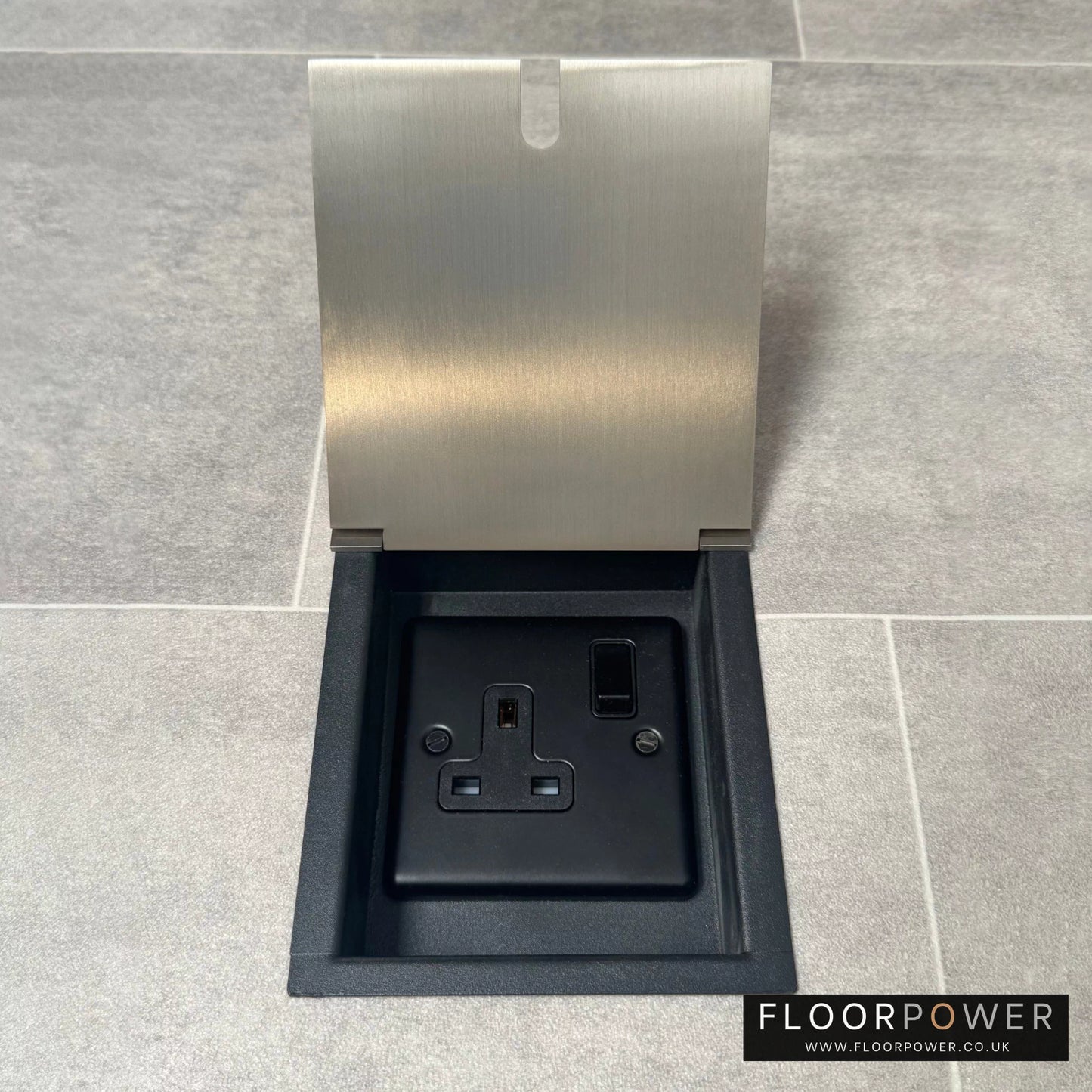 A recessed floor socket with a cover, in satin nickel finish, opened to show the 13 amp socket.