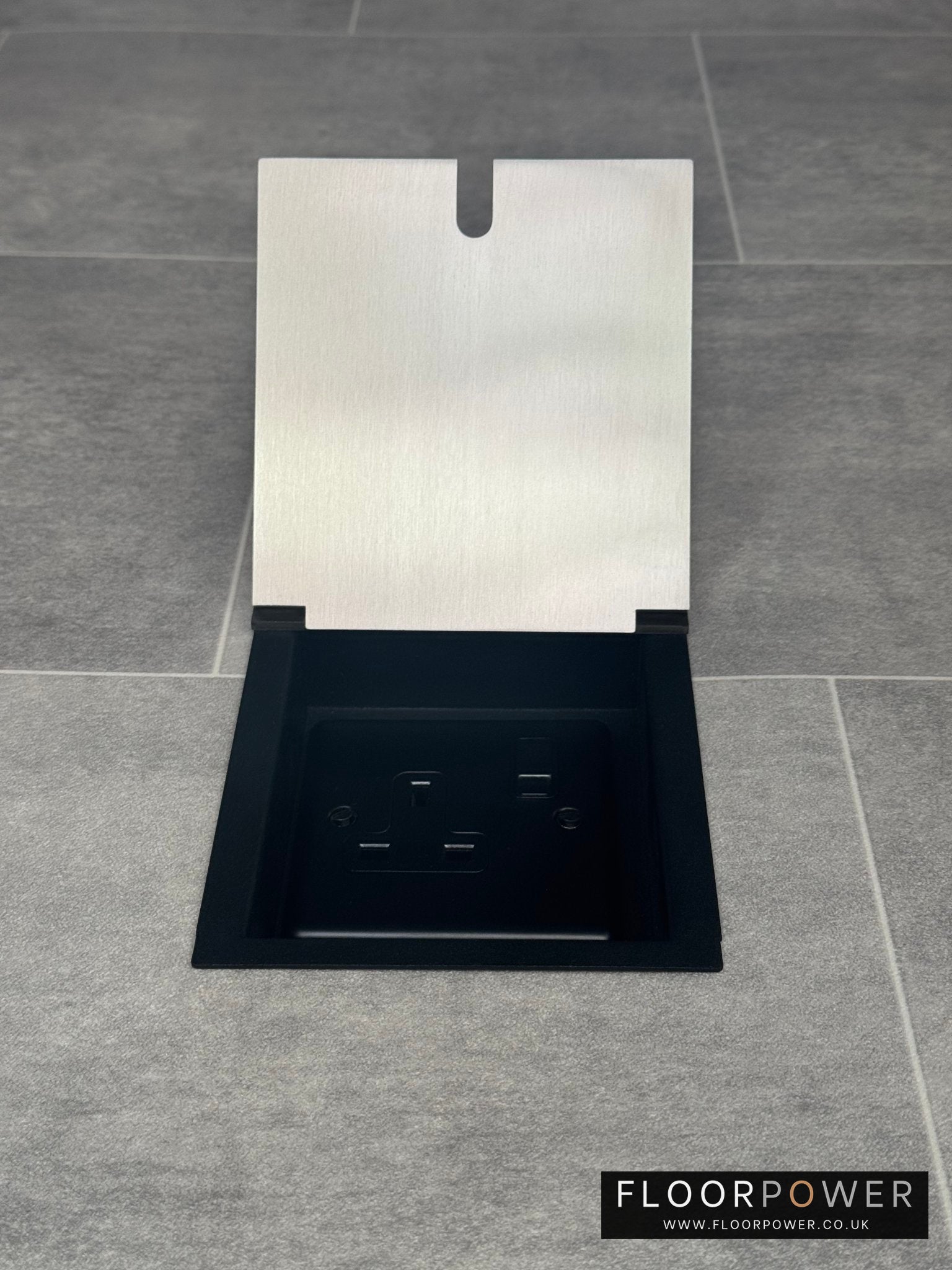 A single 13 amp plug satin stainless recessed floor socket, on a grey tiled floor.
