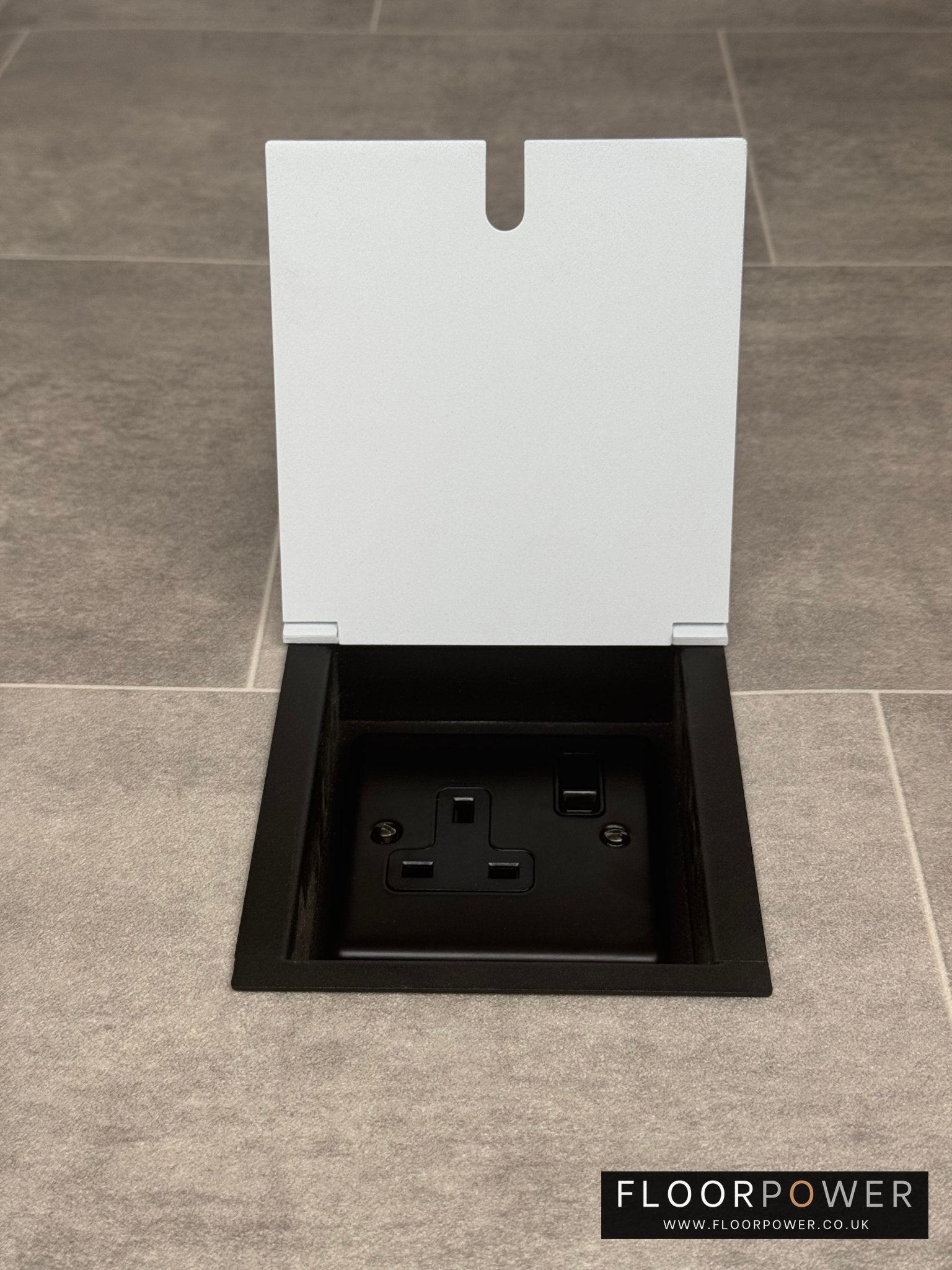 A white single recessed floor socket with one 13 amp switched socket in a black base, installed in a floor.