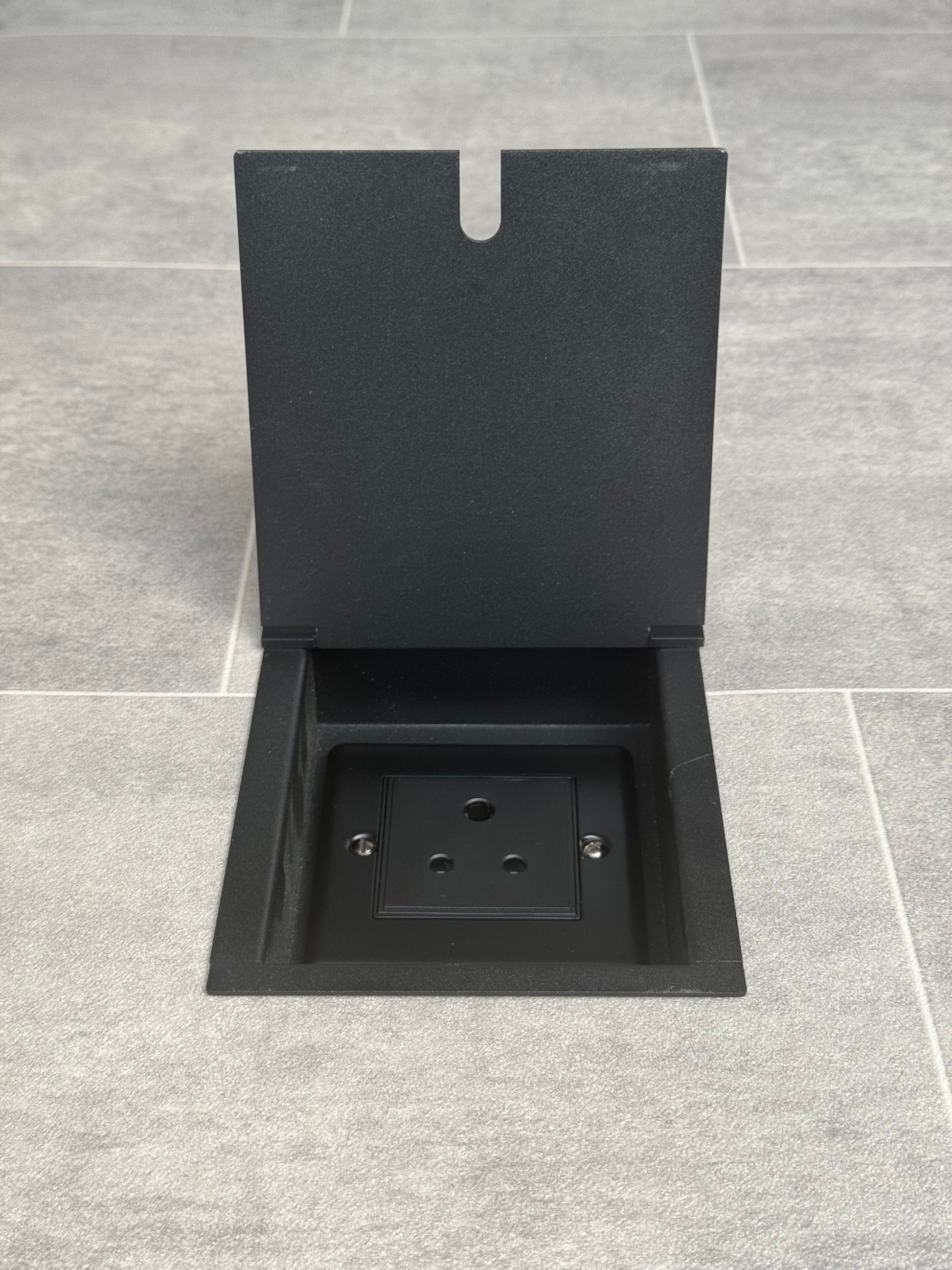 A matt black recessed floor socket with a single 5 amp round pin socket for lighting, installed in a tiled floor.