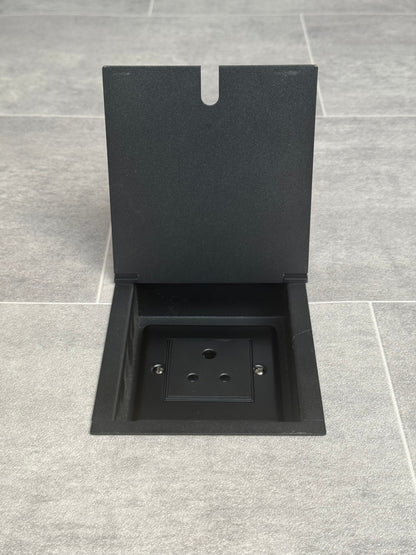 A matt black recessed floor socket with a single 5 amp round pin socket for lighting, installed in a tiled floor.