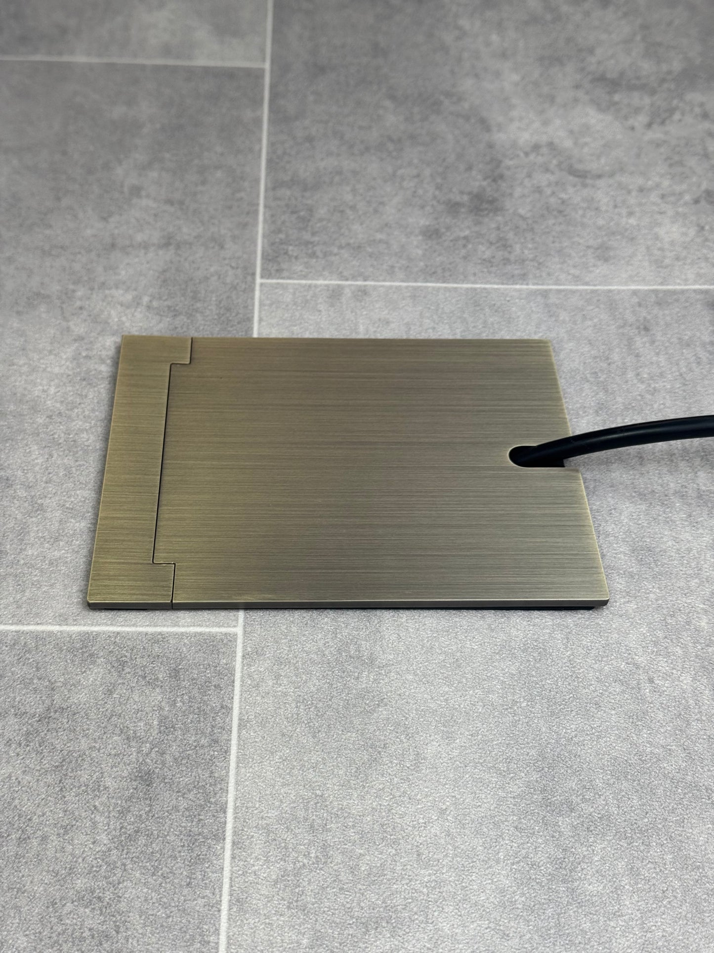 Single Antique Brass Recessed Floor Socket With Lid Closed Flat Showing Just Cable Coming Out If The Socket - Side On View.