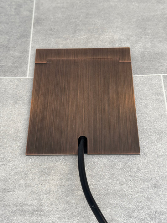 Single Antique Copper Recessed Floor Socket With Lid Closed Flat Showing Just Cable Coming Out If The Socket - Front On View.