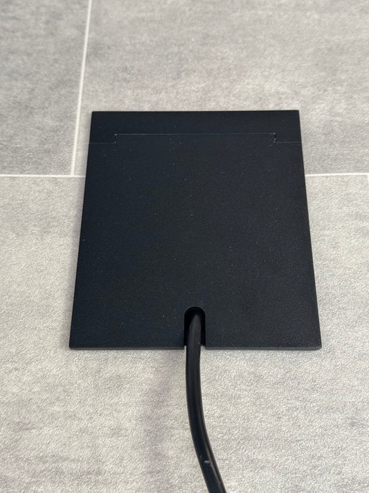 Single Matt Black Recessed Floor Socket With Lid Closed Flat Showing Just Cable Coming Out If The Socket - Front On View.
