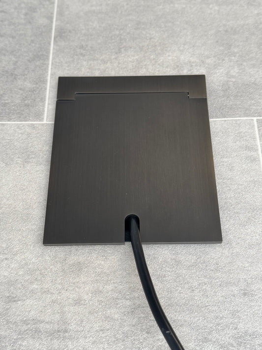 Single Old Bronze Recessed Floor Socket With Lid Closed Flat Showing Just Cable Coming Out If The Socket - Front On View.