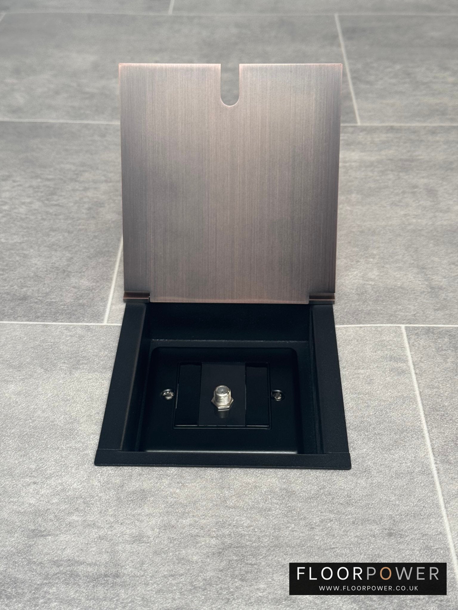 A antique copper recessed floor socket with a single satellite socket, installed on a grey floor.