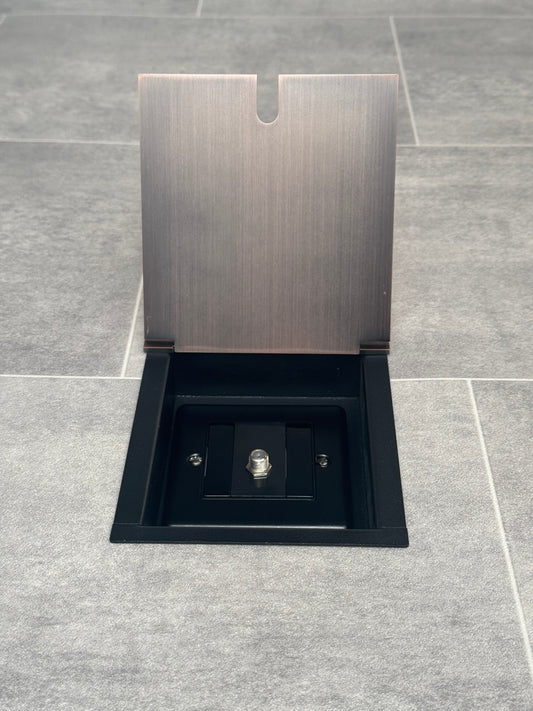 A antique copper recessed floor socket with a single satellite socket, installed on a grey floor.