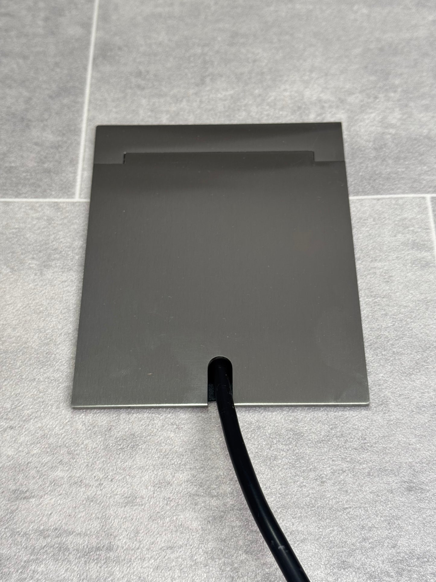 Single Satin Stainless Recessed Floor Socket With Lid Closed Flat Showing Just Cable Coming Out If The Socket - Front On View.
