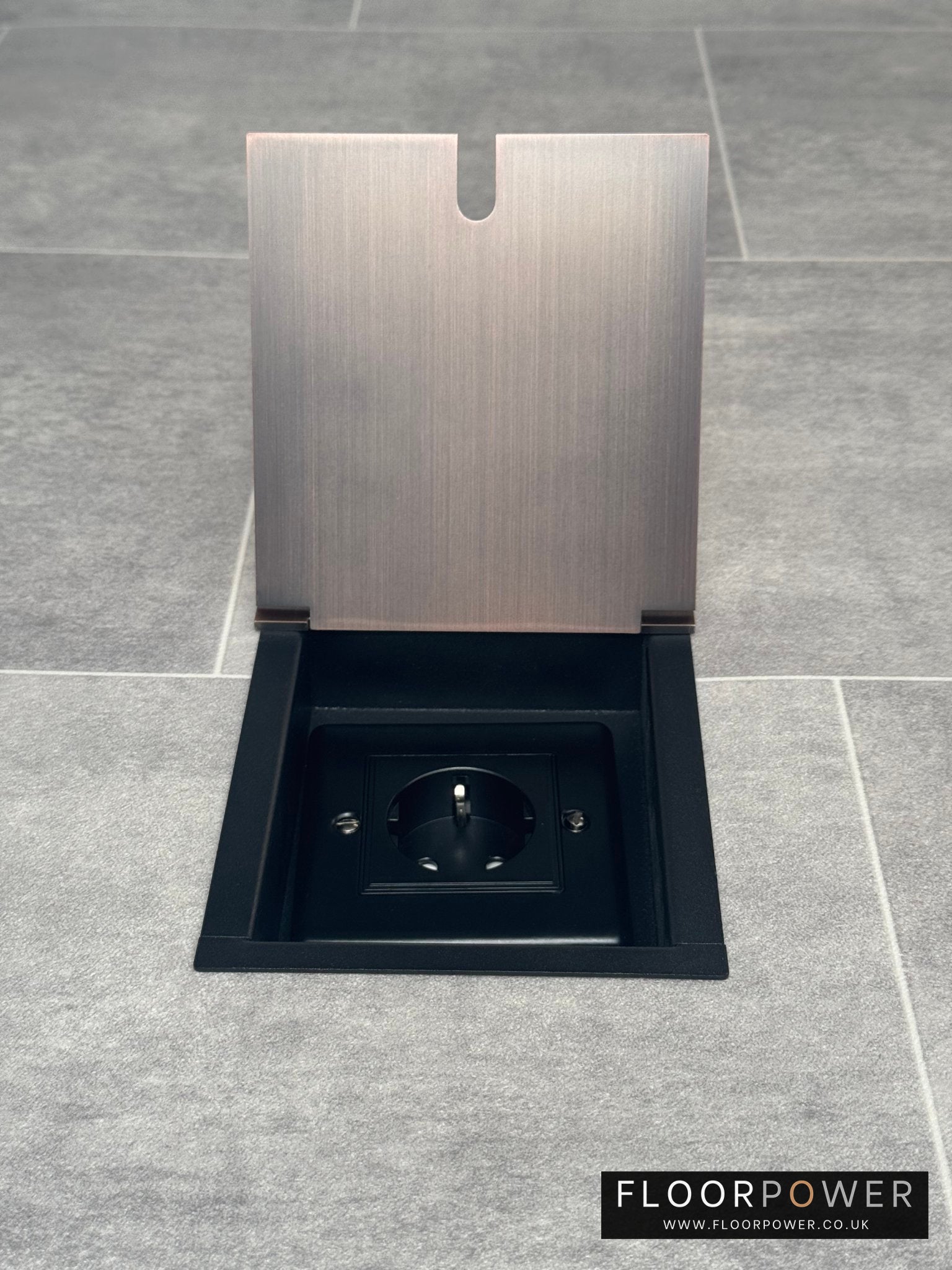 Recessed floor socket in antique copper color installed in a floor tile, with the cover opened to reveal the 13amp Schuko Socket.