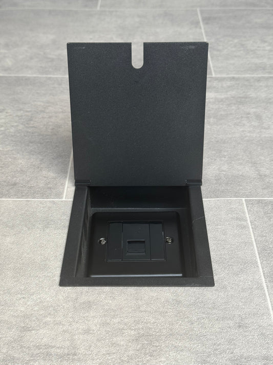 Matt black recessed floor socket with a single phone socket, shown in an open position with its cover lifted to reveal the socket.
