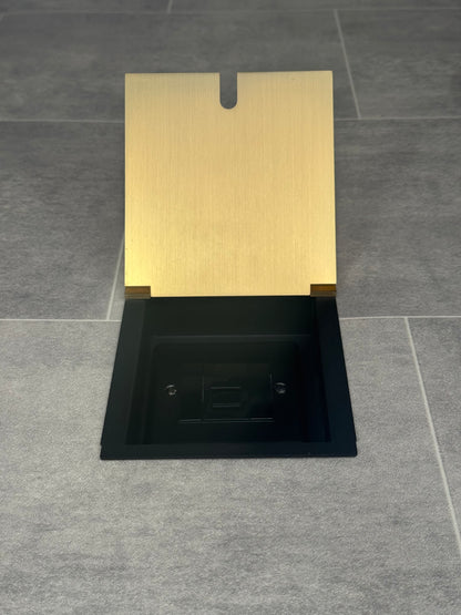 A satin brass recessed floor socket with a UK phone socket installed into a tiled floor.