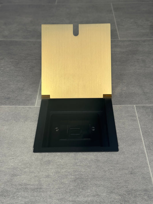 A satin brass recessed floor socket with a UK phone socket installed into a tiled floor.