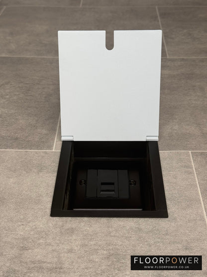 A white recessed floor socket with a UK phone socket installed on a tiled floor.