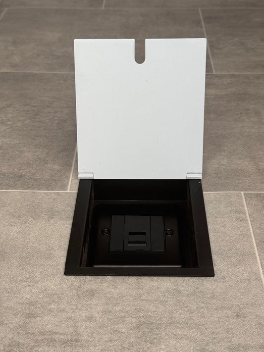 A white recessed floor socket with a UK phone socket installed on a tiled floor.