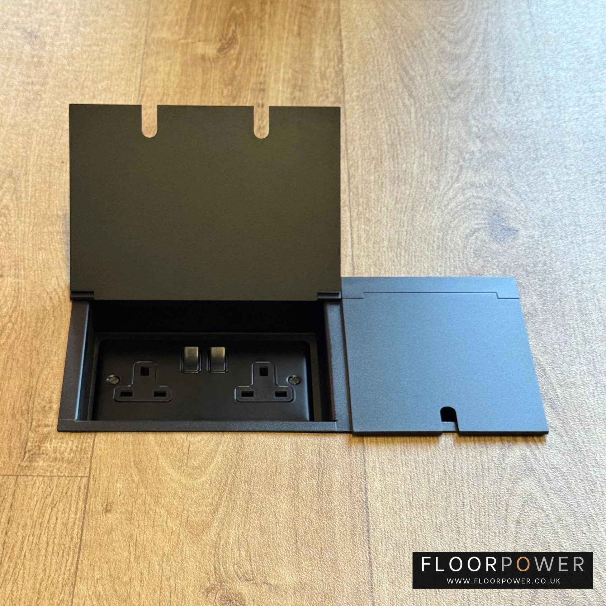 Triple Recessed Floor Socket in Matt Black on a wood floor, with double side lid open showing plug socket.